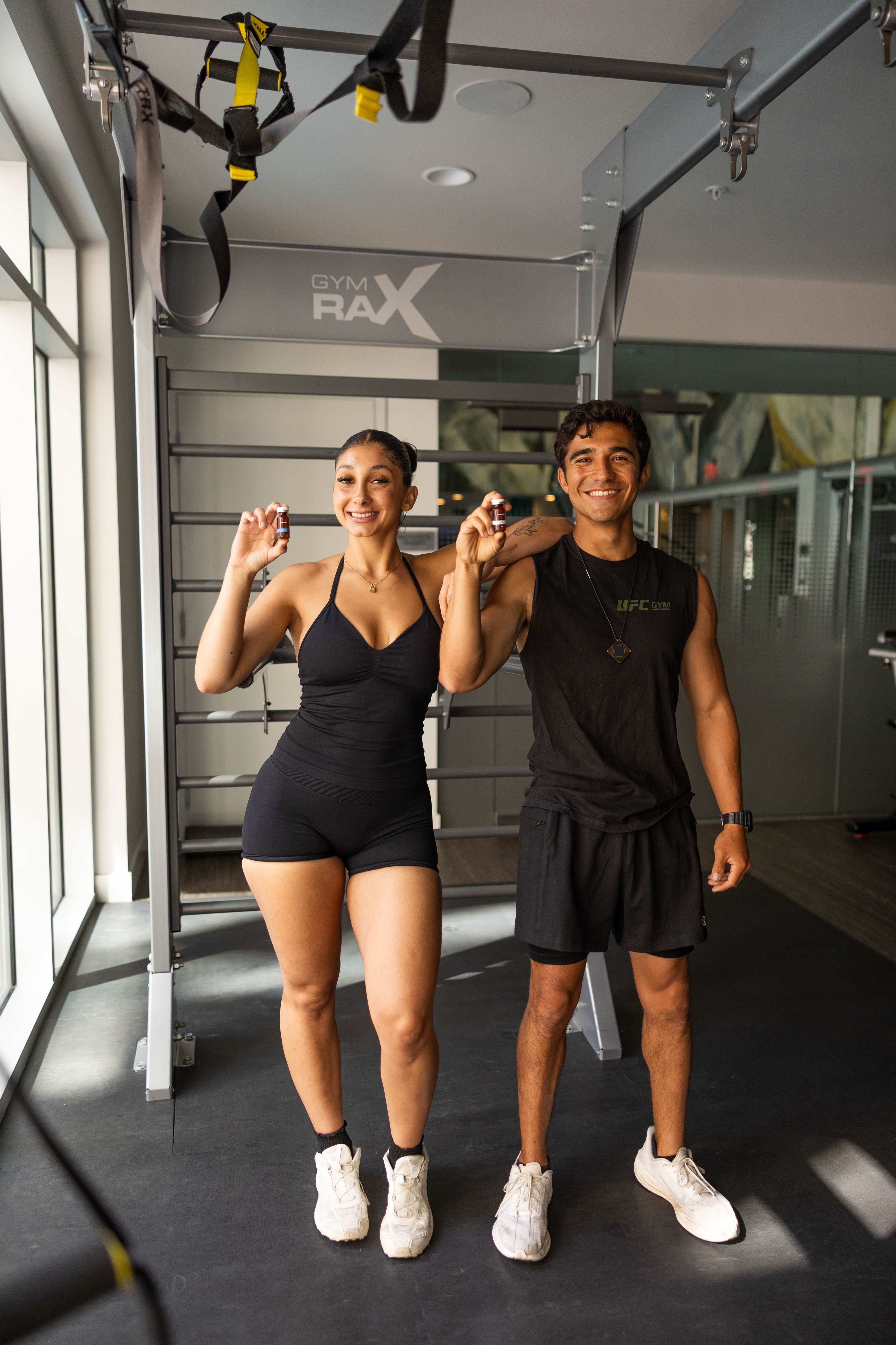 Two athletes smiling in the gym, each holding a Buena Health peptide vial